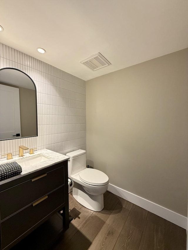 half bath with vanity, toilet, tile walls, wood finished floors, and visible vents