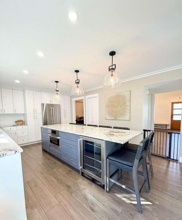 kitchen featuring decorative light fixtures, light stone countertops, beverage cooler, stainless steel appliances, and white cabinetry