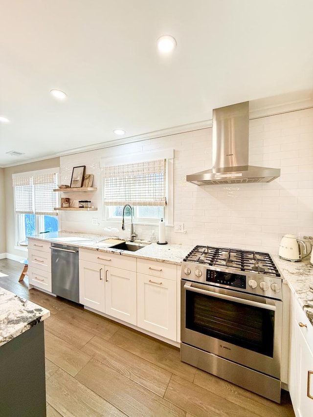 kitchen with light stone countertops, appliances with stainless steel finishes, a sink, wall chimney exhaust hood, and decorative backsplash