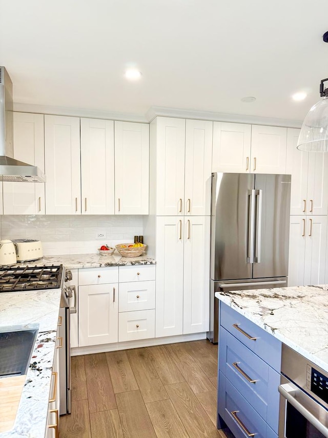 kitchen featuring blue cabinetry, appliances with stainless steel finishes, light wood-type flooring, white cabinets, and wall chimney exhaust hood