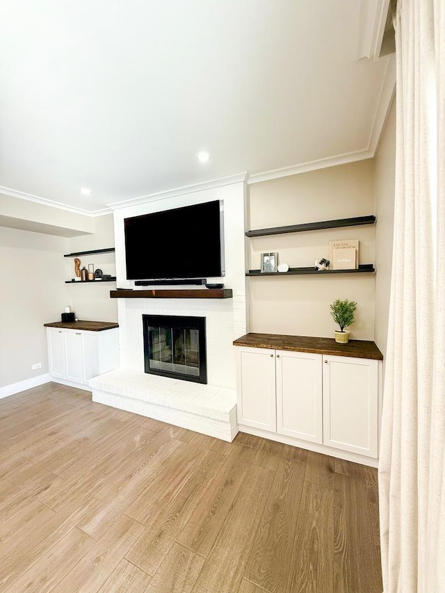 unfurnished living room with ornamental molding, a brick fireplace, and light wood-style flooring