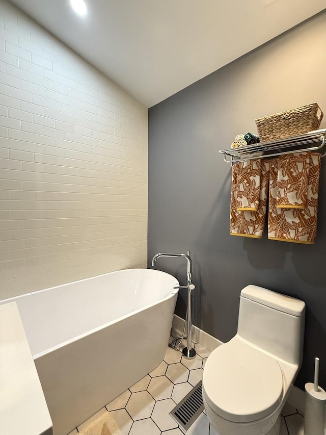bathroom featuring toilet, tile patterned floors, a freestanding tub, lofted ceiling, and visible vents