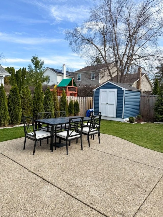 view of patio / terrace with fence, a storage unit, outdoor dining space, and an outbuilding