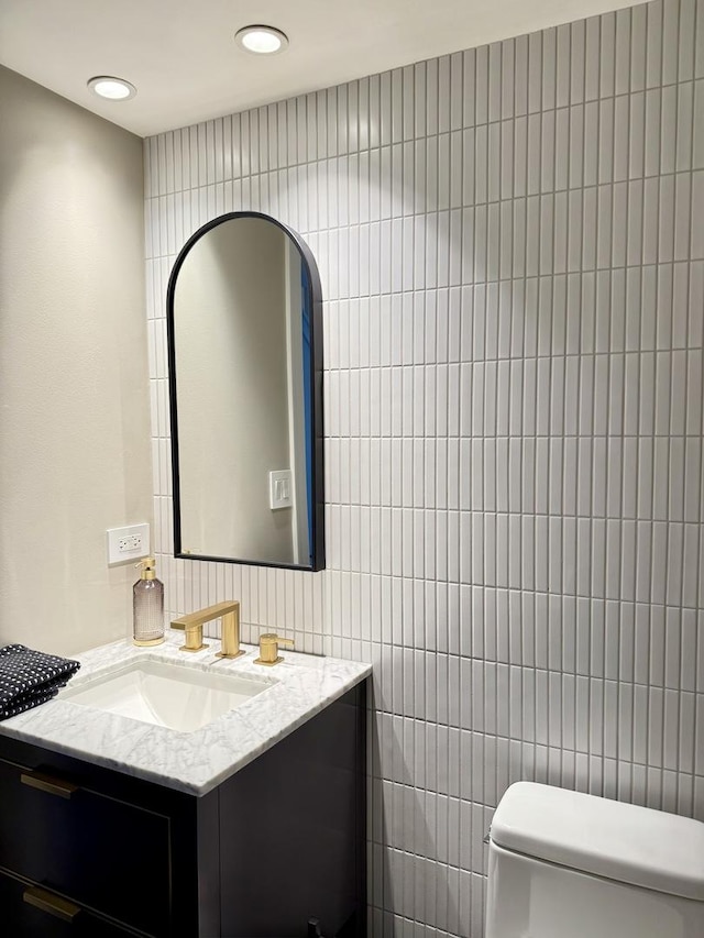 half bath featuring vanity, recessed lighting, toilet, and tile walls