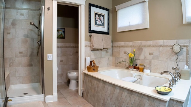 full bathroom featuring a stall shower, toilet, tile patterned flooring, a bath, and tile walls