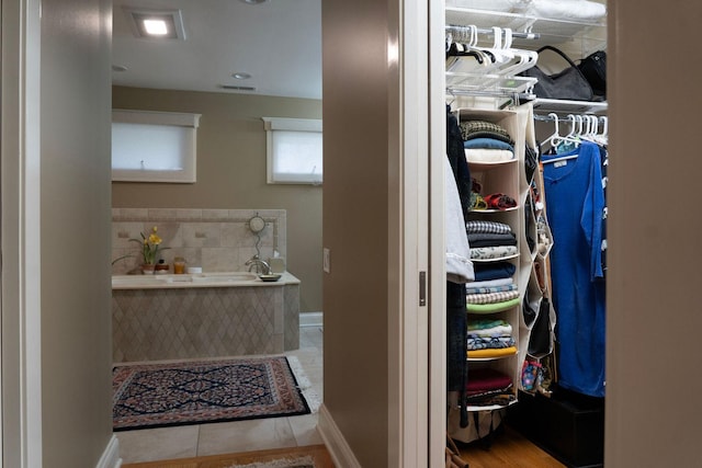 bathroom featuring a walk in closet, a bath, baseboards, and tile patterned floors