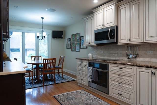 kitchen featuring stainless steel microwave, wall oven, black electric stovetop, light wood-style flooring, and a chandelier