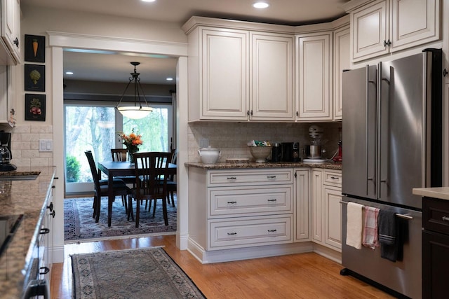 kitchen with freestanding refrigerator, backsplash, light wood-style flooring, light stone counters, and pendant lighting