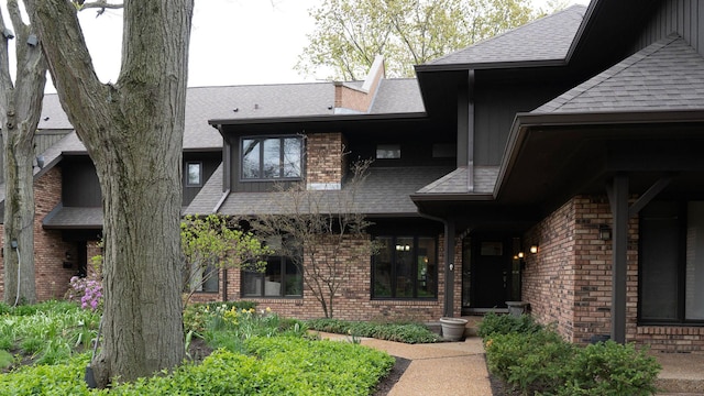 doorway to property featuring brick siding, a shingled roof, and board and batten siding