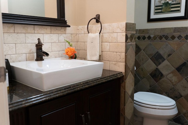 half bathroom featuring tile walls, vanity, toilet, and wainscoting