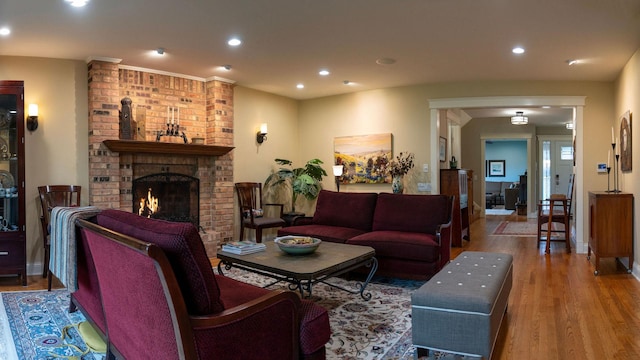 living room with wood finished floors, a brick fireplace, recessed lighting, and arched walkways