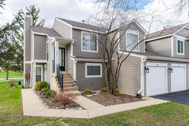 view of front of home with driveway, a chimney, entry steps, an attached garage, and a front yard