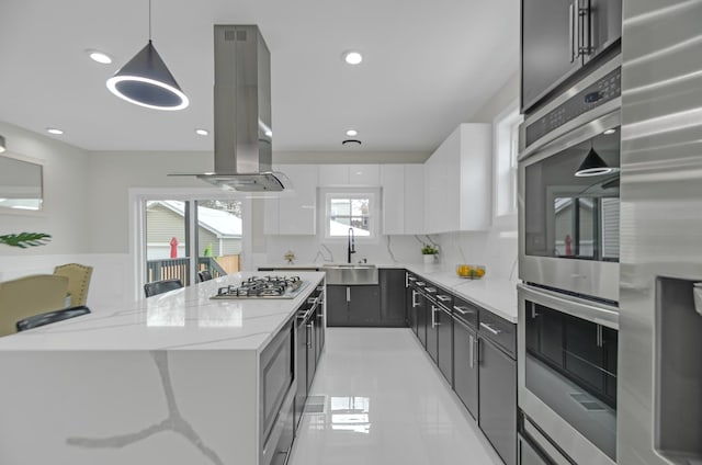 kitchen with a sink, appliances with stainless steel finishes, white cabinetry, island exhaust hood, and light stone counters