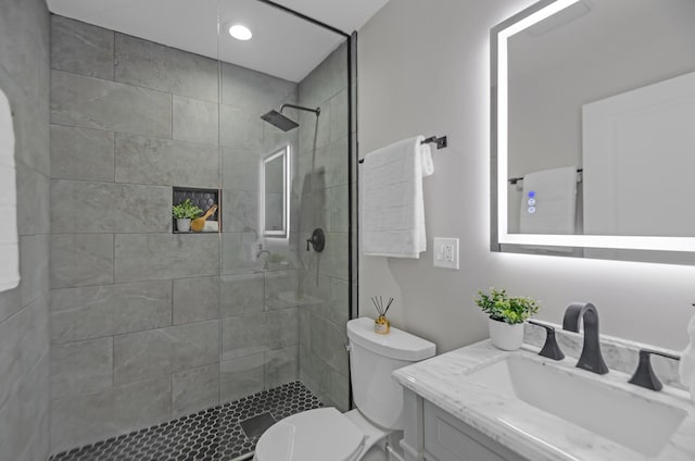 bathroom with toilet, a tile shower, and vanity