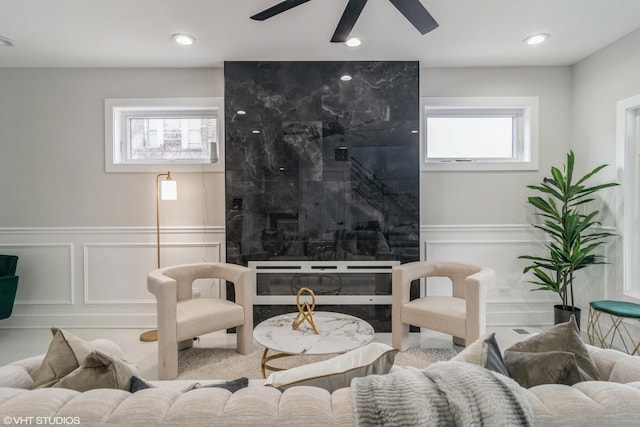 living room featuring a decorative wall, wainscoting, a ceiling fan, and a healthy amount of sunlight