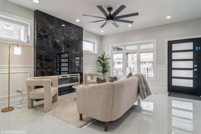 living area featuring a ceiling fan, a decorative wall, wainscoting, and recessed lighting