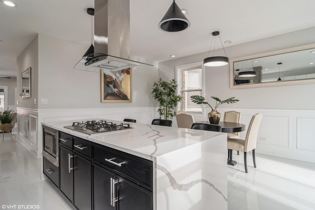 kitchen featuring a decorative wall, dark cabinets, a wainscoted wall, island exhaust hood, and stainless steel appliances