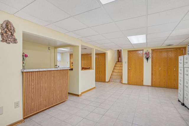 unfurnished room with baseboards, a paneled ceiling, bar area, and stairway