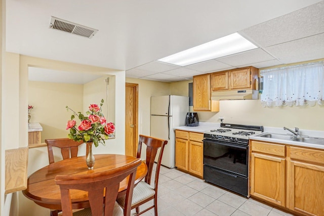 kitchen featuring under cabinet range hood, range with gas cooktop, visible vents, light tile patterned floors, and freestanding refrigerator