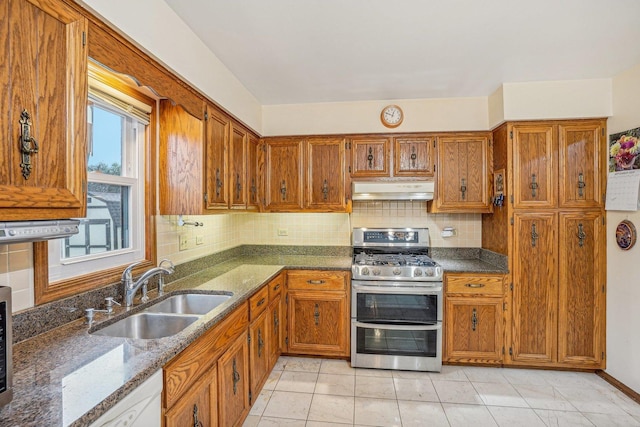 kitchen featuring under cabinet range hood, a sink, double oven range, decorative backsplash, and brown cabinetry
