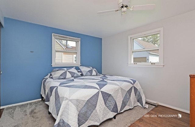bedroom with ceiling fan, baseboards, wood finished floors, and multiple windows