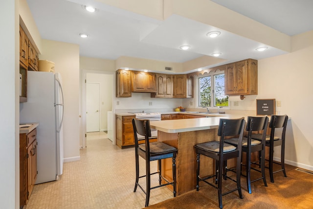 kitchen with white appliances, a peninsula, brown cabinets, and baseboards