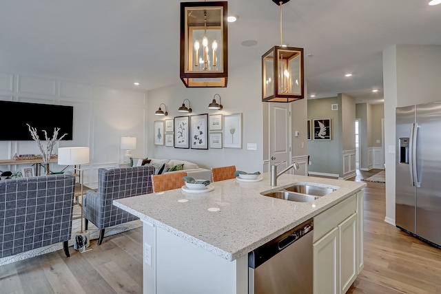 kitchen featuring light stone counters, light wood-style flooring, appliances with stainless steel finishes, a decorative wall, and a sink