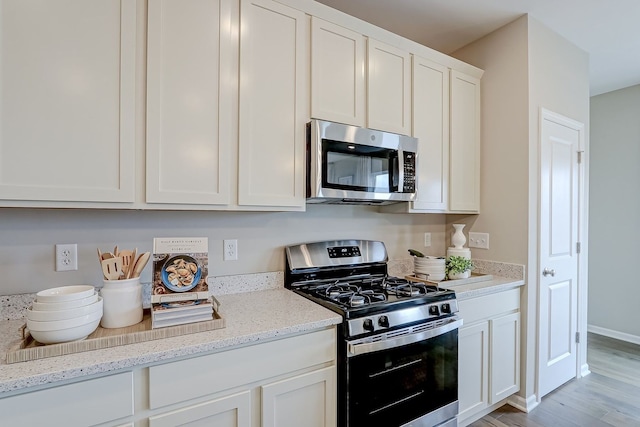 kitchen featuring light wood-type flooring, white cabinets, appliances with stainless steel finishes, and light stone countertops