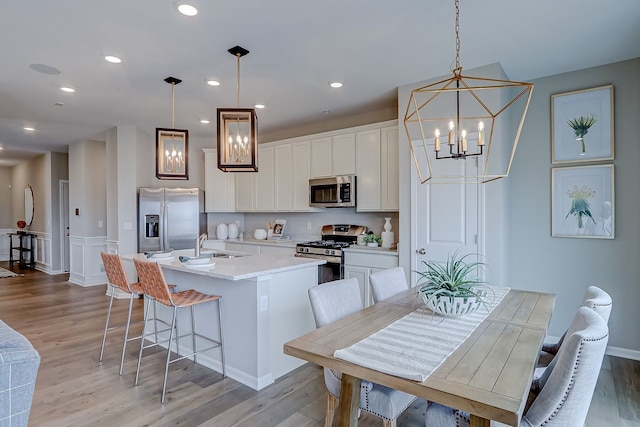 kitchen with light wood-style flooring, white cabinets, appliances with stainless steel finishes, a kitchen island with sink, and a sink
