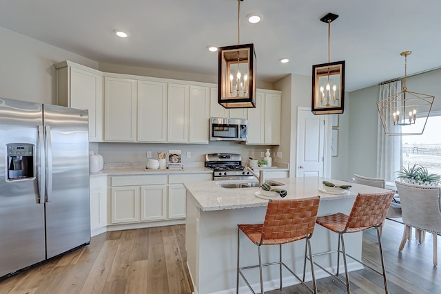 kitchen with white cabinets, a sink, a chandelier, light wood finished floors, and stainless steel appliances