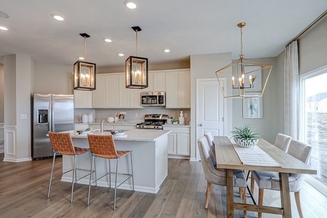 kitchen featuring a center island with sink, appliances with stainless steel finishes, an inviting chandelier, and white cabinetry