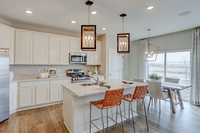 kitchen with an inviting chandelier, a sink, white cabinetry, stainless steel appliances, and light wood-style flooring