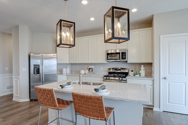 kitchen with appliances with stainless steel finishes, wood finished floors, a sink, and white cabinets