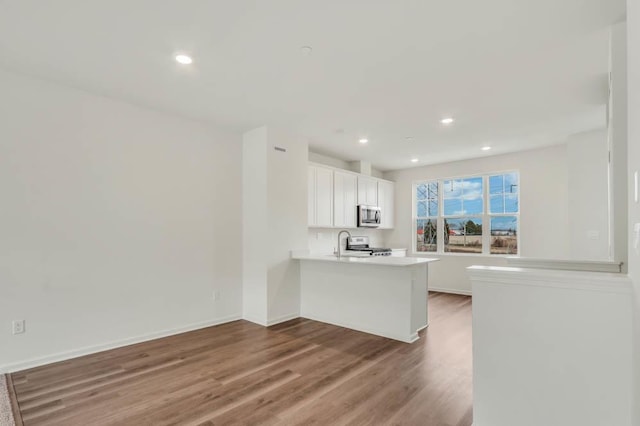kitchen featuring a peninsula, light countertops, white cabinets, stainless steel appliances, and wood finished floors