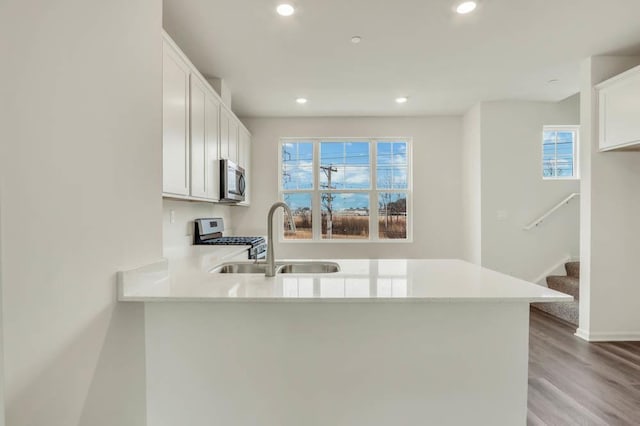kitchen with a sink, a peninsula, recessed lighting, stainless steel appliances, and light wood-style flooring