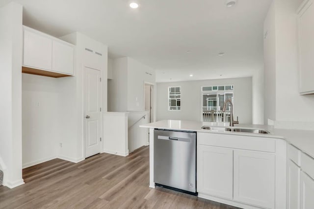 kitchen featuring a peninsula, white cabinets, dishwasher, a sink, and light wood finished floors