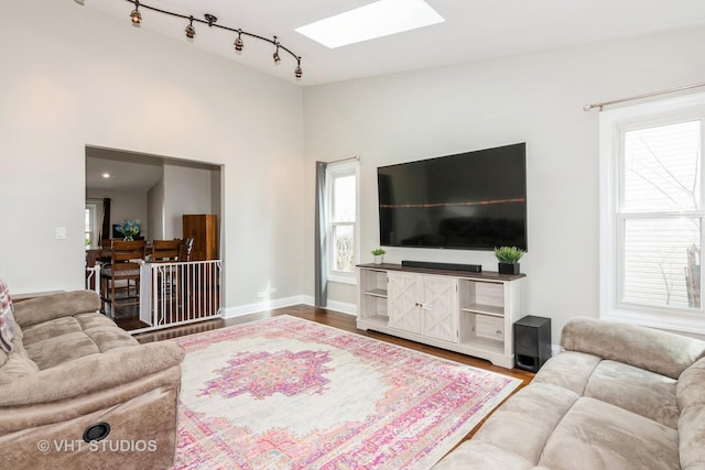 living room with plenty of natural light, track lighting, wood finished floors, and a skylight