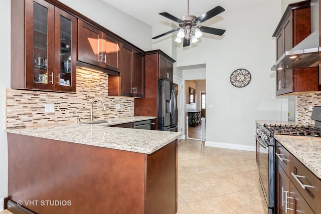 kitchen featuring a sink, wall chimney range hood, stainless steel appliances, decorative backsplash, and light stone counters
