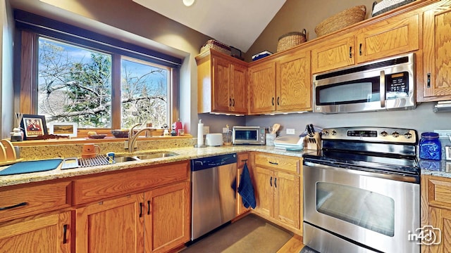 kitchen featuring lofted ceiling, appliances with stainless steel finishes, light stone countertops, and a sink