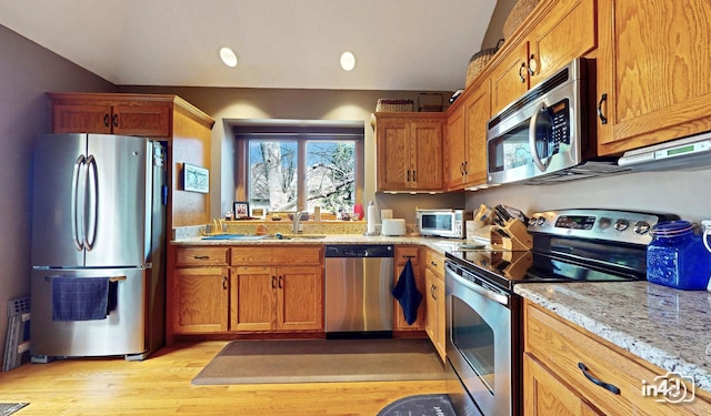 kitchen featuring appliances with stainless steel finishes, light stone countertops, a sink, and light wood-type flooring