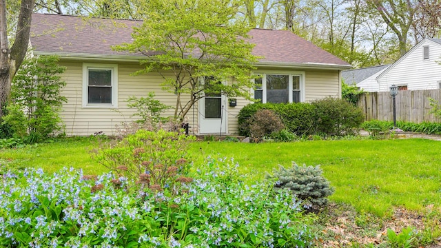 rear view of property featuring a yard, roof with shingles, and fence