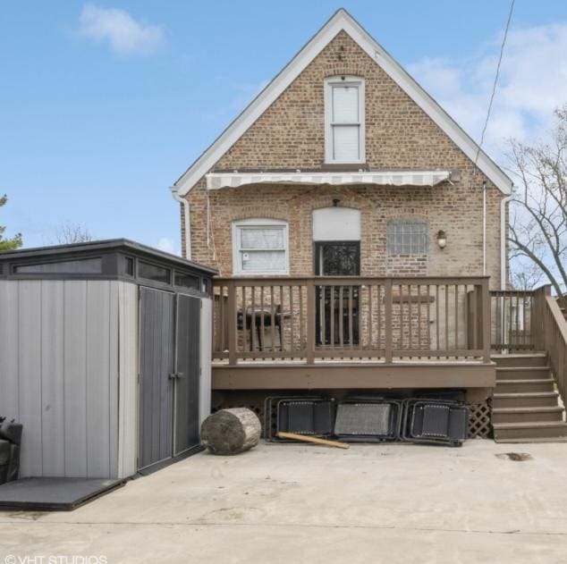 rear view of property with a wooden deck, a storage shed, brick siding, and an outdoor structure