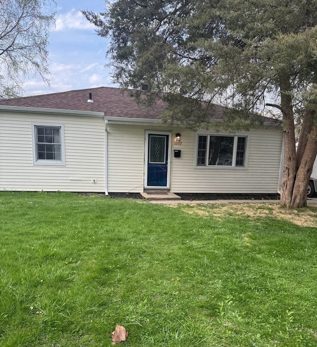 view of front of home with entry steps, roof with shingles, and a front lawn