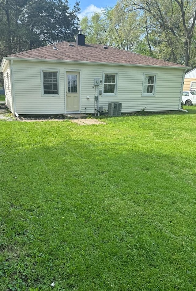 rear view of property with a lawn, a chimney, and central AC