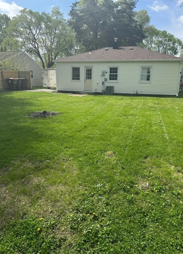 rear view of property with a lawn, central AC, and fence