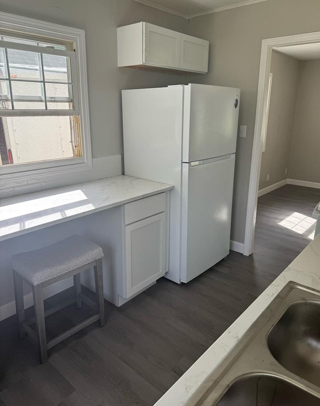 kitchen featuring dark wood-style flooring, light stone countertops, white cabinets, freestanding refrigerator, and ornamental molding