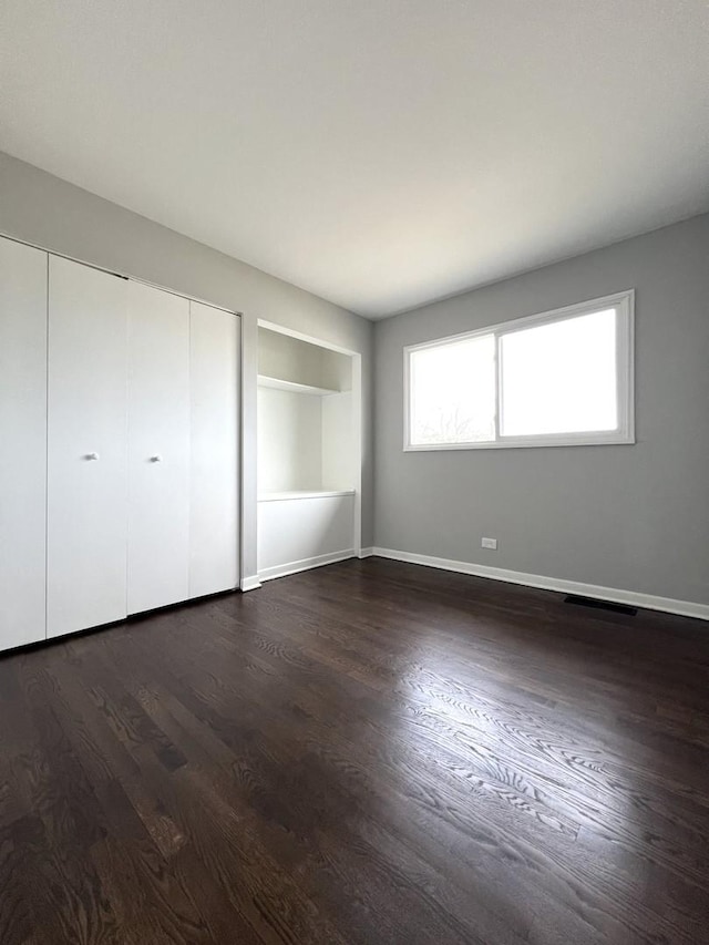 unfurnished bedroom with dark wood-type flooring, a closet, and baseboards