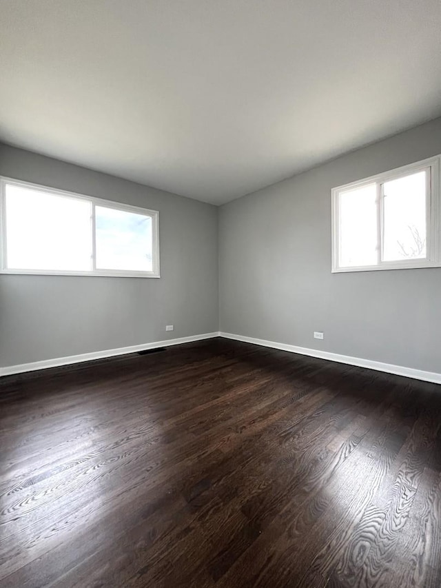 unfurnished room featuring a wealth of natural light, dark wood-style floors, and baseboards