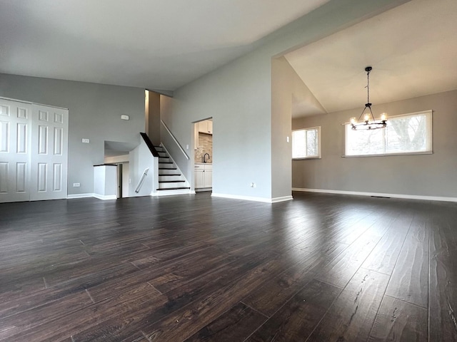 unfurnished living room featuring baseboards, a notable chandelier, dark wood finished floors, stairs, and lofted ceiling