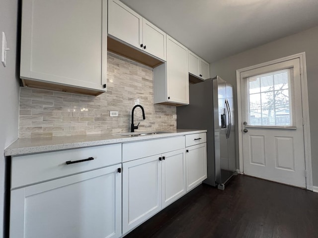 kitchen with light stone countertops, dark wood-style floors, white cabinetry, a sink, and backsplash